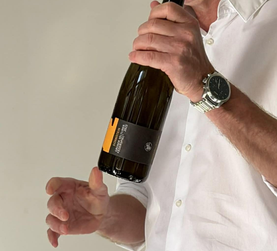 En mand i skjort holder en flaske durnstein gruner veltliner