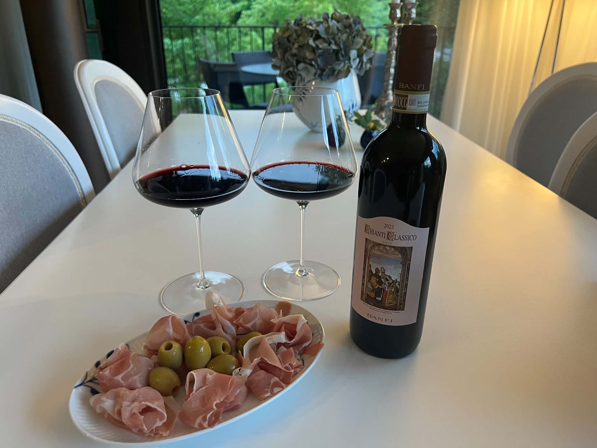 2 vinglas og en tallerken med mad på, ved siden af en flaske Castello Banfi Chianti Classico