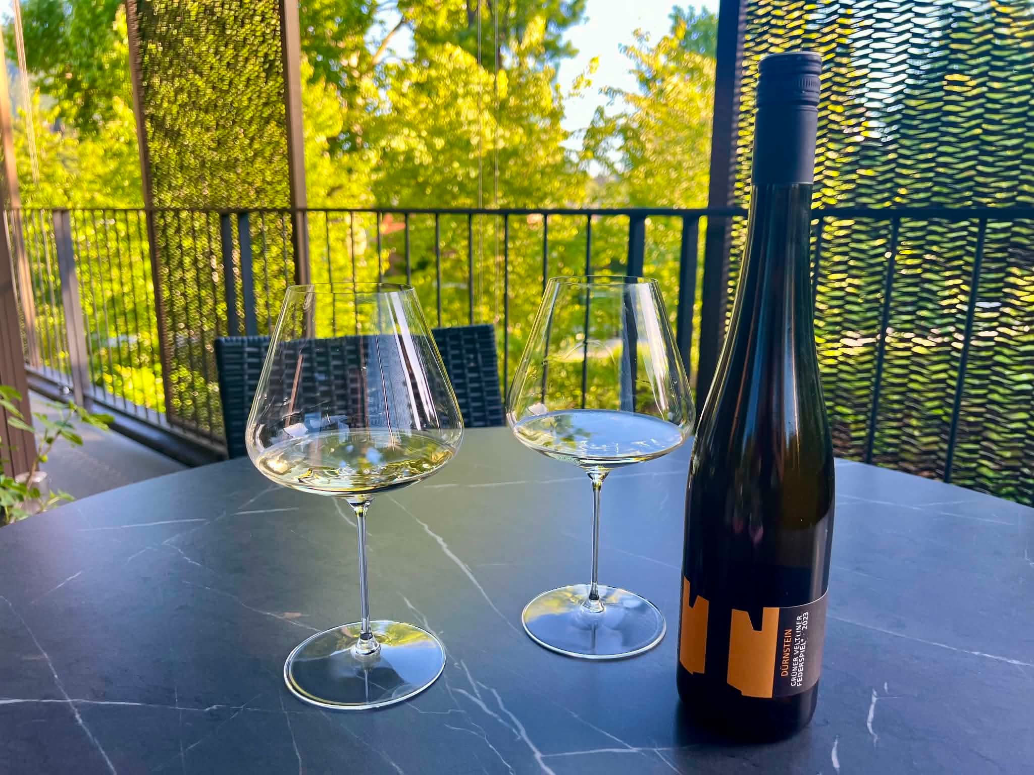 En flaske Tegernseerhof durnstein gruner veltliner med 2 vinglas på et terrrassebord